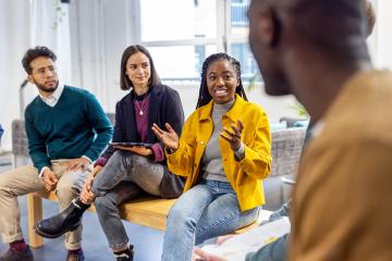 African woman talking with colleagues sitting in circle at a coworking office.