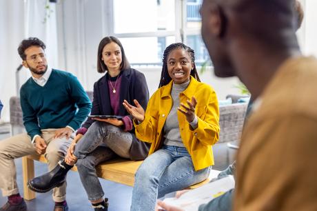 African woman talking with colleagues sitting in circle at a coworking office.